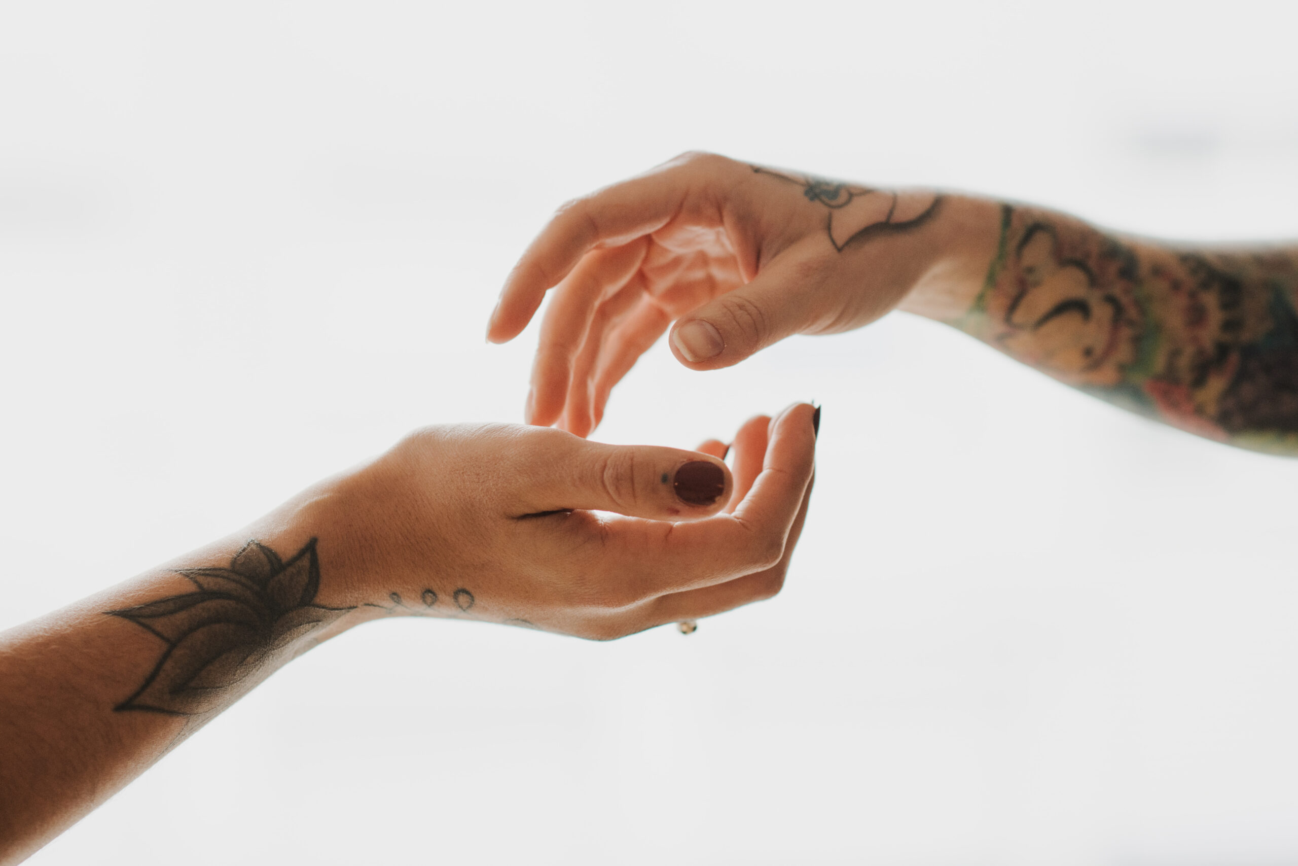 Berührung – Die Kunst der Verbindung Zwei tätowierte Hände nähern sich einander in einem Moment der Berührung. Die feinen Details der Tattoos und die sanfte Haltung der Finger symbolisieren Vertrauen, Nähe und kreative Ausdruckskraft – ein Leitmotiv des Atelier Lumina Mannheim.